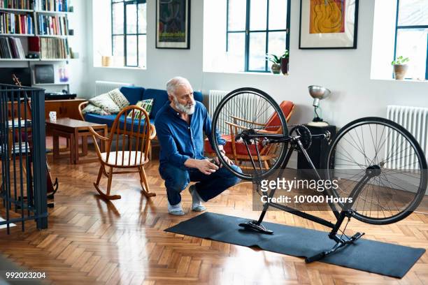 active senior man repairing bike in apartment - tyre stockfoto's en -beelden