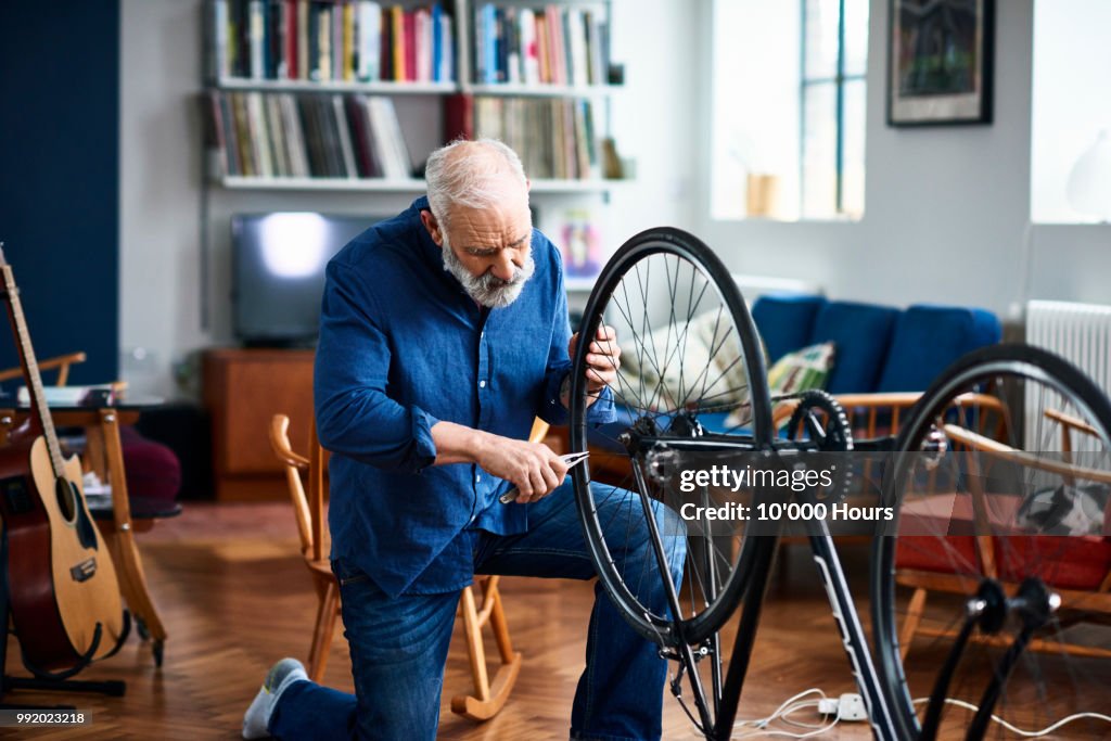 Senior man fixing bike using pliers to repair wheel