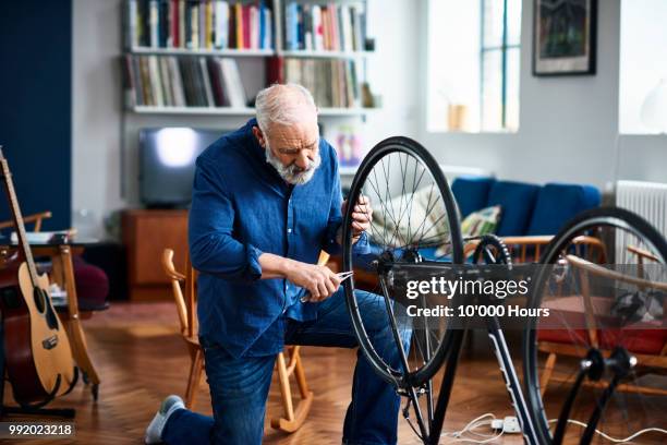 senior man fixing bike using pliers to repair wheel - bijstellen stockfoto's en -beelden