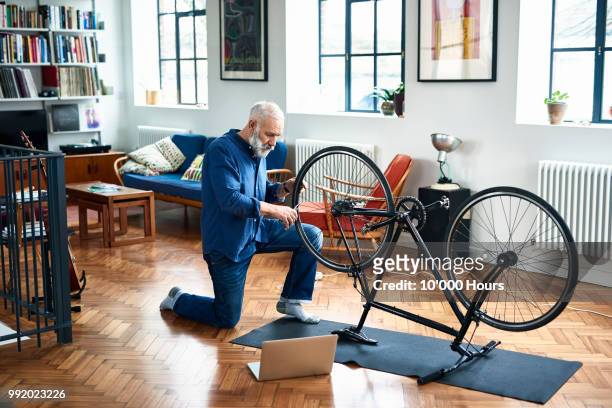 senior man repairing bicycle on floor in apartment - pieno di risorse foto e immagini stock