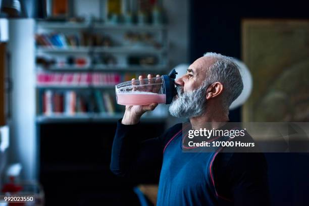 senior man wearing sports top gulping health drink from container - drinking juice stock-fotos und bilder