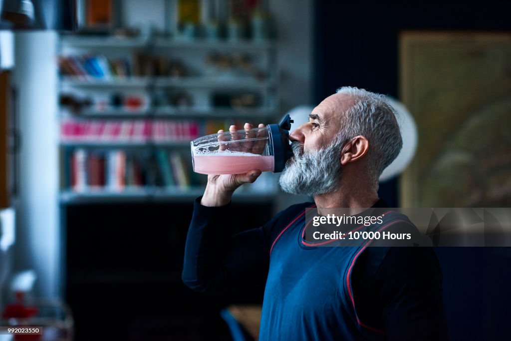 Senior man wearing sports top gulping health drink from container