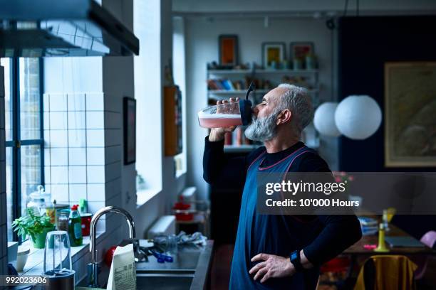 senior man drinking nutritional sports drink by kitchen sink - nutritional supplement stockfoto's en -beelden