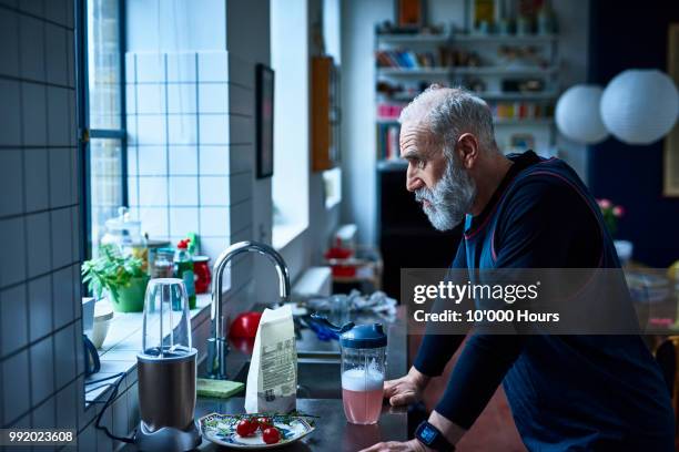 tired looking senior man leaning on kitchen counter with sports drink - missing emotion 個照片及圖片檔