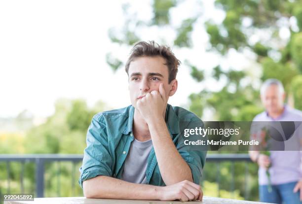 a young man is leaning on a table as another man approaches - androgynous boys stock-fotos und bilder