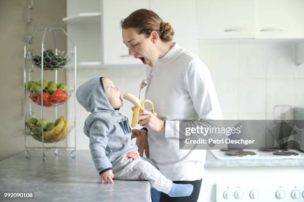 a young mother sharing a banana with her baby. - petri schaal stockfoto's en -beelden