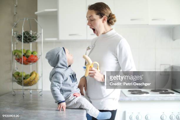 a young mother sharing a banana with her baby. - petri schaal stockfoto's en -beelden