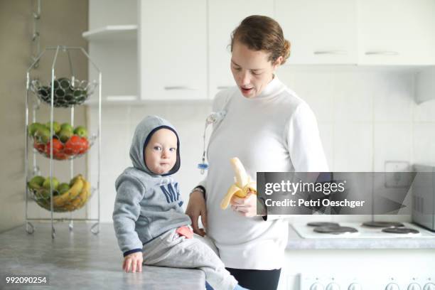 a young mother sharing a banana with her baby. - petri schaal stockfoto's en -beelden