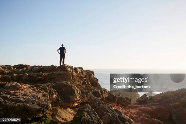 silhouette of man standing on cliff by sea against sky - klippe stock-fotos und bilder