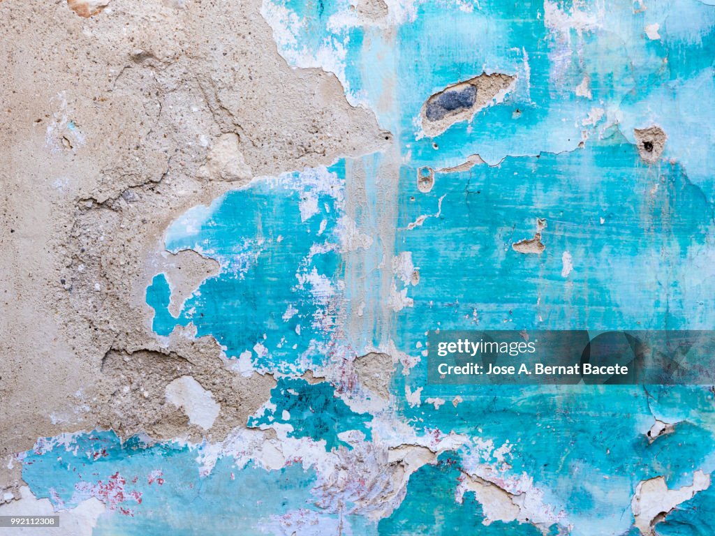 Wall with peeling blue and white paint with cracks and dampness.