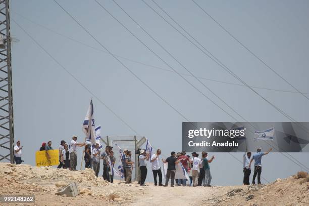 Jewish settlers wave flags and shout slogans while Israeli forces raise security as Palestinians keep watch in Khan al-Ahmar village following...