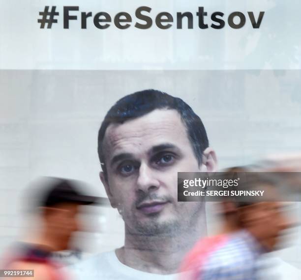 People walk past a poster with the hashtag 'freesentsov' and a photo of Ukrainian film director Oleg Sentsov, taken by journalist Anton Naumlyuk, and...