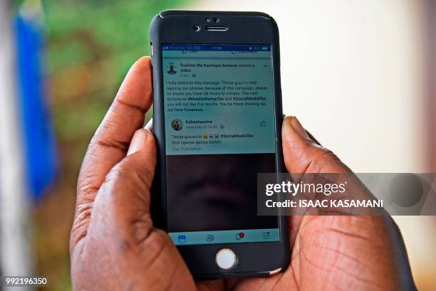 Woman reads a message on social media tax as she scrolls through her Facebook account on her phone in Kampala on July 5, 2018. - Politicians,...