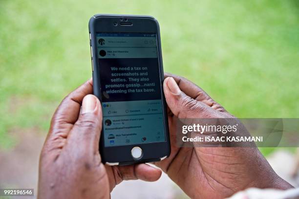 Woman reads a message on social media tax as she scrolls through her Facebook account on her phone in Kampala on July 5, 2018. - Politicians,...