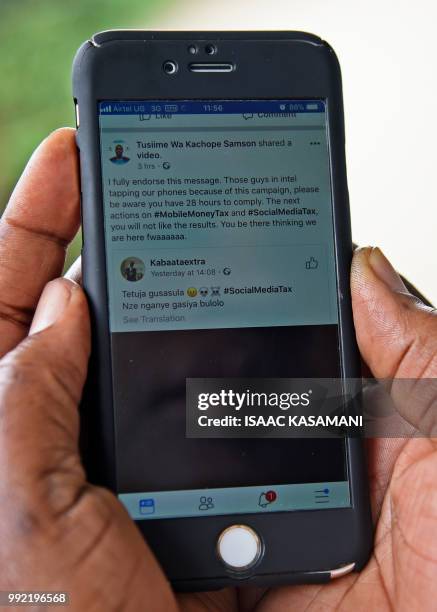 Woman reads a message on social media tax as she scrolls through her Facebook account on her phone in Kampala on July 5, 2018. - Politicians,...