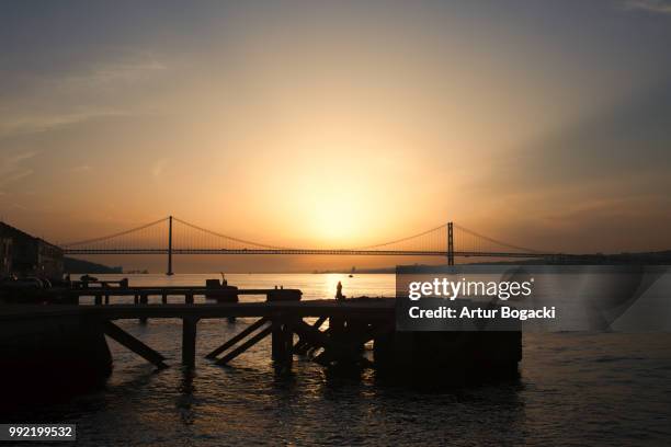 sunset at almada quay and 25 de abril bridge in lisbon - abril 個照片及圖片檔