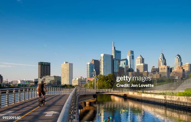 schuylkill river park boardwalk with cyclist and philadelphia skyline at sunset - schuylkill river photos et images de collection
