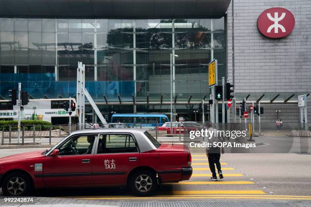 Commuter crosses the road towards MTR subway station and next to a taxi in Central district, Hong Kong.