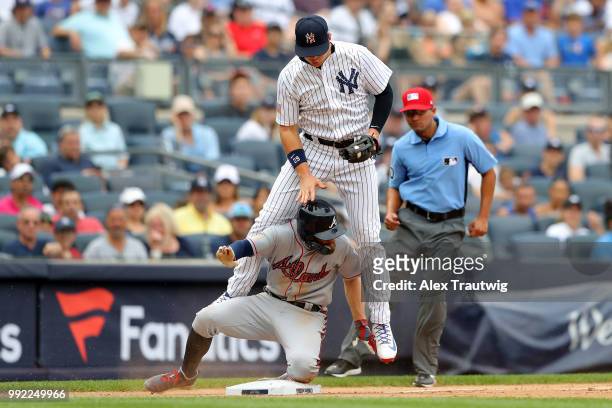 Brandon Drury of the New York Yankees jumps as Ender Inciarte of the Atlanta Braves slides into third base during a game at Yankee Stadium on...
