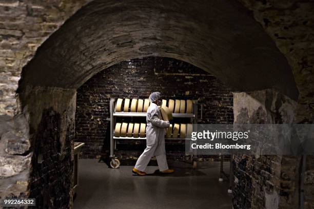 Worker carries a BellaVitano cheese wheel to rub with black pepper at the Sartori Cheese factory in Plymouth, Wisconsin, U.S., on Tuesday, July 3,...