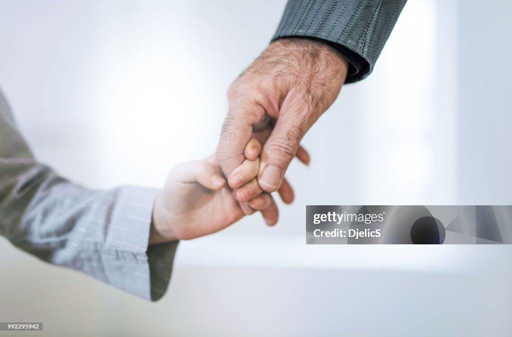 Hand close-up of grandfather and granddaughter holding hands.