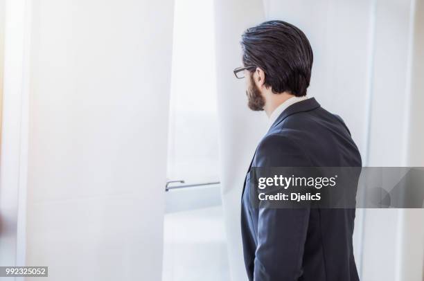 young businessman looking through the window and contemplating about life. - unhappy salesman stock pictures, royalty-free photos & images