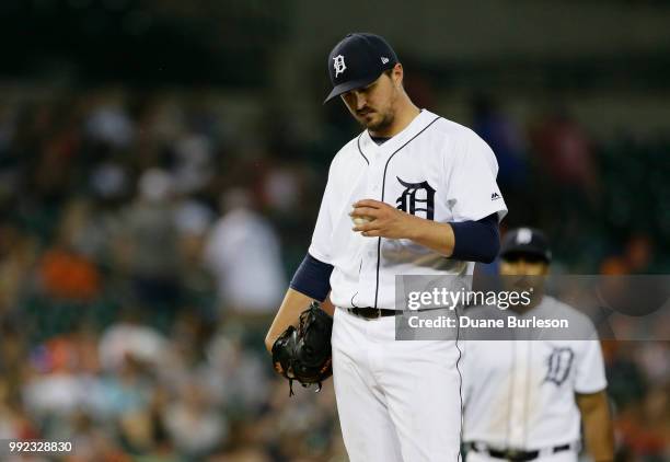 Starting pitcher Blaine Hardy of the Detroit Tigers looks at a baseball as manager Ron Gardenhire of the Detroit Tigers heads for the mound to pull...