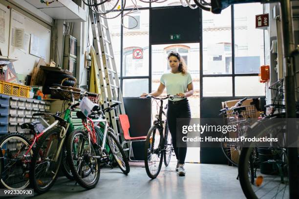 young woman bringing bicycle in for repair - hinterhaus stockfoto's en -beelden