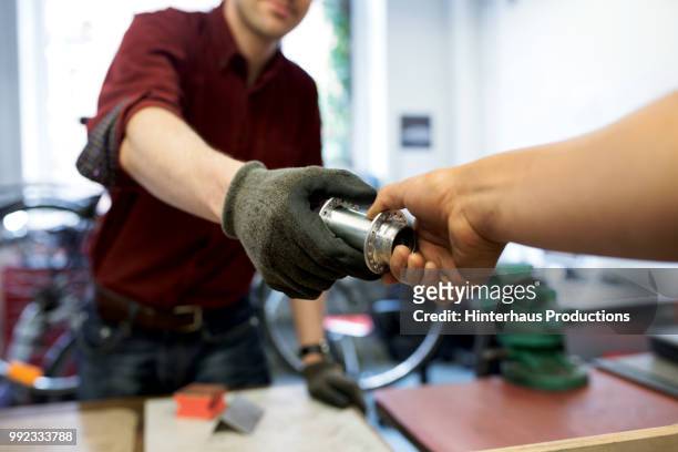 bike mechanic handing bicycle part to colleague - car parts stock pictures, royalty-free photos & images