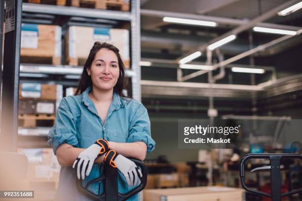 portrait of young worker leaning on pallet jack at warehouse - beroep stockfoto's en -beelden