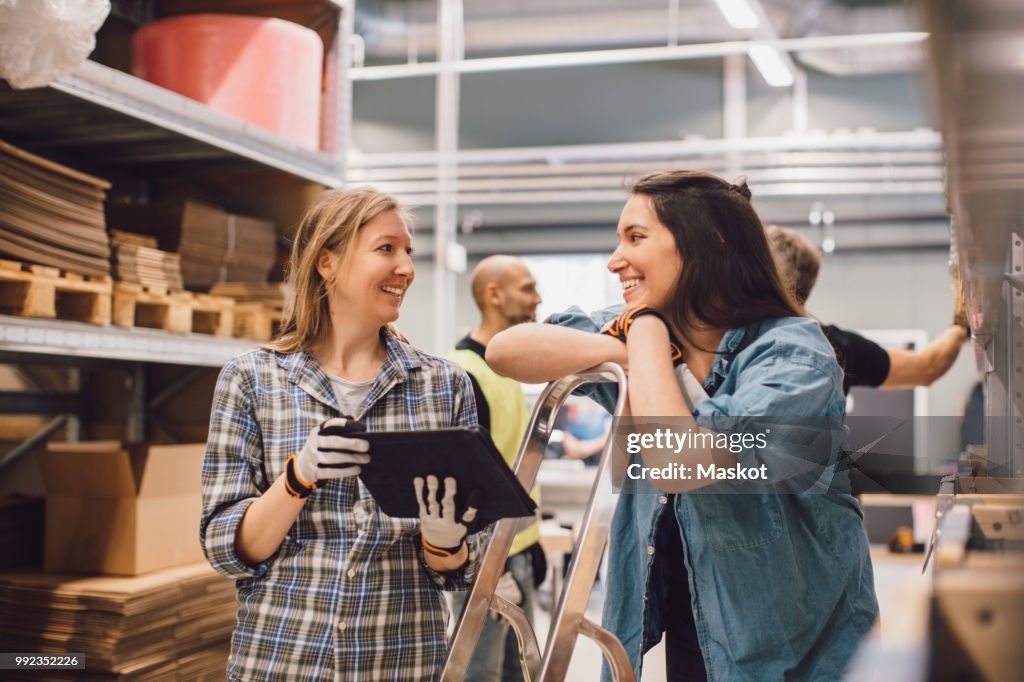 Smiling woman showing digital tablet to female colleague while men working in background