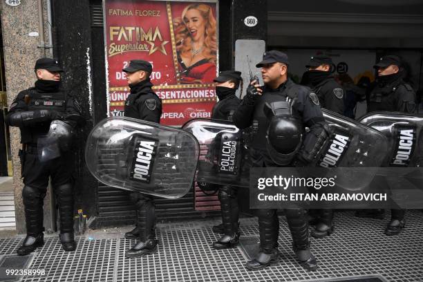 Police officers keep watch as workers of state-owned news agency Telam and colleagues demonstrate in Buenos Aires on July 5, 2018 against a mass...