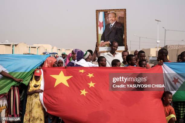 People hold Chinese and Djiboutian national flags with the portrait of Djibouti's President Ismail Omar Guellehas as they wait for the arrival of the...