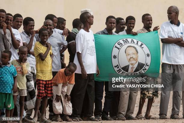 People hold a flag of Djibouti's President Ismail Omar Guellehas as they wait for the arrival of the President before the launching ceremony of new...