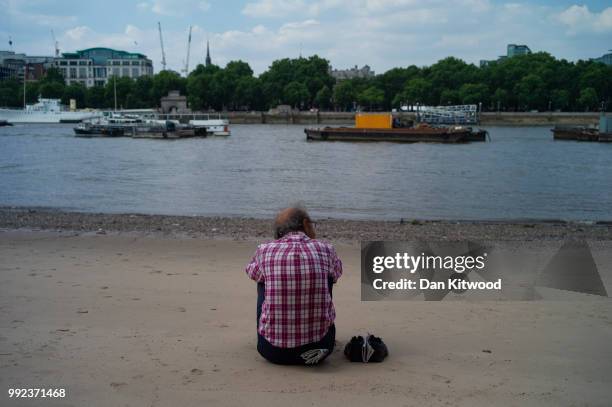 Man sits on a beach created at low tide on the Thames on July 5, 2018 in London, England. A prolonged heatwave continues to grip much of the country,...