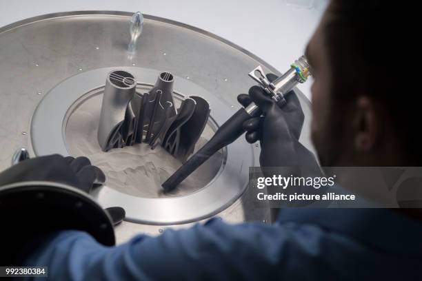 An employee vacuumes metall powder from a 3D printed component at an unpacking station at the 3D printing application centre of the machine...