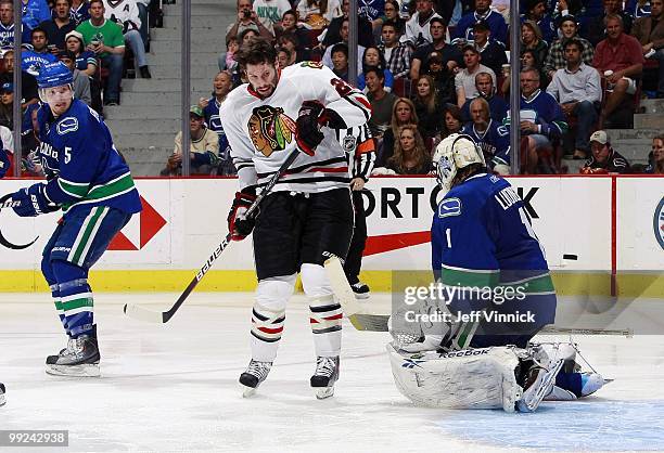 Christian Ehrhoff of the Vancouver Canucks and a helmetless Troy Brouwer of the Chicago Blackhawks look on as Roberto Luongo of the Vancouver Canucks...