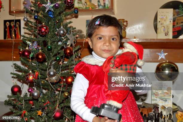 pakistani little christian girl holding santa claus (toy) in her arms and enjoying the christmas in her home - amir mukhtar stock pictures, royalty-free photos & images