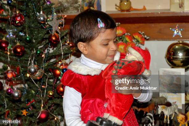 pakistani little christian girl holding santa claus (toy) in her arms and enjoying the christmas in her home - amir mukhtar stock pictures, royalty-free photos & images