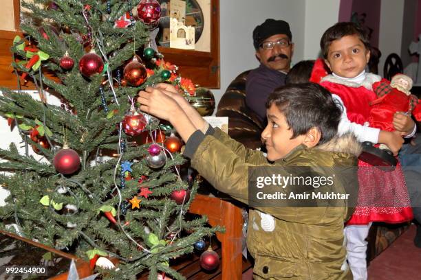 a little pakistani boy decorating christmas tree on the eve of christmas 2017 at his home in the presence of his father and sister - amir mukhtar stock pictures, royalty-free photos & images