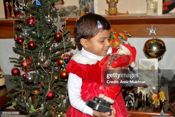 pakistani little christian girl holding santa claus (toy) in her arms and enjoying the christmas in her home - amir mukhtar stock pictures, royalty-free photos & images