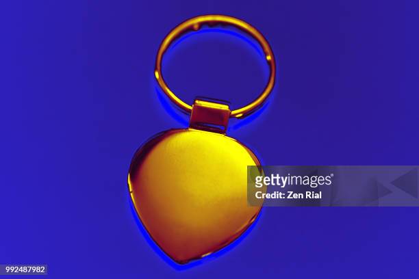 color manipulated image of a gold colored heart-shaped metal key ring  glows against blue background - key ring isolated stockfoto's en -beelden