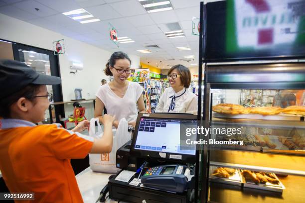 An employee serves customers at a check out counter of a 7-Eleven store in Ho Chi Minh City, Vietnam, on Wednesday, June 20, 2018. For decades,...