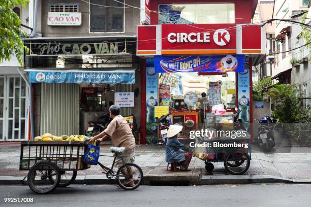 Fruit vendor sits waiting for customers at her cart as a fellow fruit vendor walks past outside a Circle K store in Ho Chi Minh City, Vietnam, on...