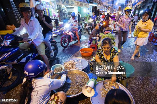 Motorcyclists pass vendors preparing and sell seafood in a market at night in Ho Chi Minh City, Vietnam, on Wednesday, June 20, 2018. For decades,...