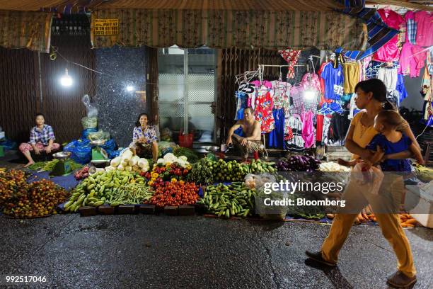 Pedestrian carrying a baby walks past vendors selling fruit and vegetables in a market at night in Ho Chi Minh City, Vietnam, on Wednesday, June 20,...