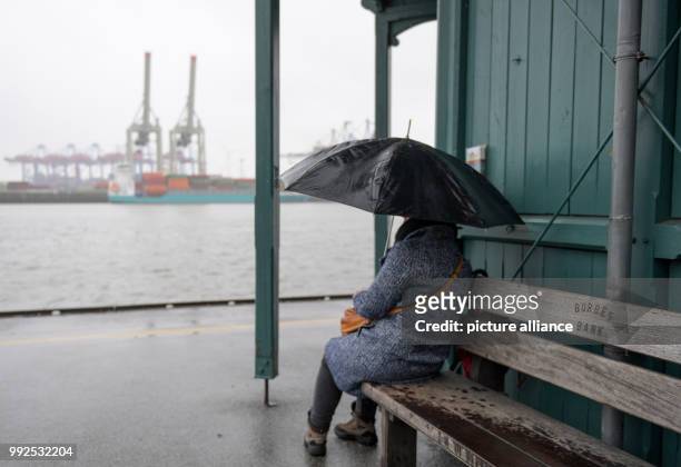Woman with an umbrella waiting during pouring rain for the departure of a harbour ferry at the museums port Ovelgoenne in Hamburg, Germany, 22...