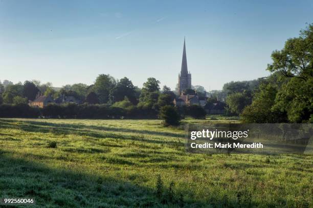 early summer morning shadows sweep a field in burford in the cotswolds - kirchturmspitze stock-fotos und bilder