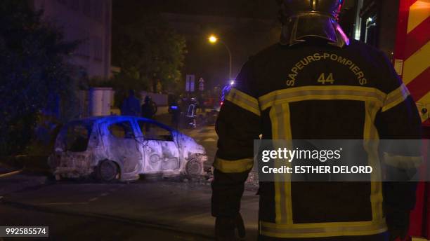 This grab taken from video images, shows emergency service workers as they look at a burnt-out vehicle on a street in Nantes early July 6, 2018. -...