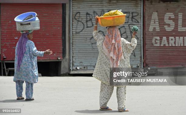 Indian Kashmiri women carry containers outside the Jamia Masjid mosque after authorities imposed restrictions in downtown Srinagar on July 6, 2018. -...